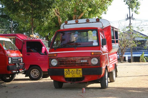 Dos tuk-tuks rojos de Phuket, pequeñas furgonetas con matrícula amarilla, aparcados a la sombra