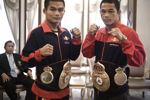 Dos boxeadores tailandeses con cinturones de campeón y chaquetas rojas y negras con el logotipo de Krating Daeng