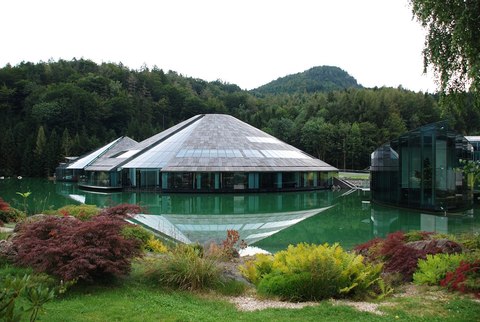 Edificios de cristal con forma piramidal sobre un estanque, rodeados de bosque, en la sede de Red Bull en Austria