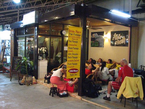 Clientes recibiendo masaje de pies en sillones a la entrada de un local de masajes