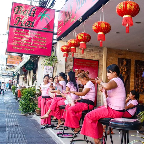 Masajistas sentadas en la acera frente a un local de masajes con carteles de precios