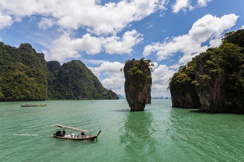 La roca de Ko Tapu saliendo del agua verde de la bahía de Phang Nga, con una barca longtail delante