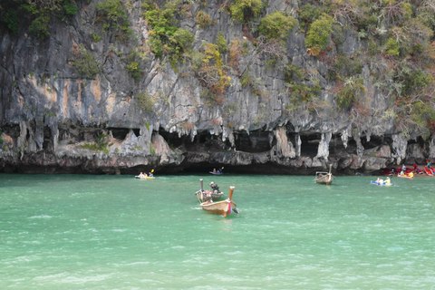Canoas y una barca longtail en el agua verde junto a los acantilados de las islas Hong